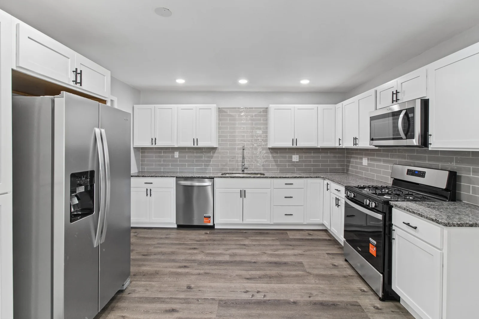 1239 Maple St kitchen with white cabinets, gray tile backsplash, stainless steel appliances and wood-look flooring.