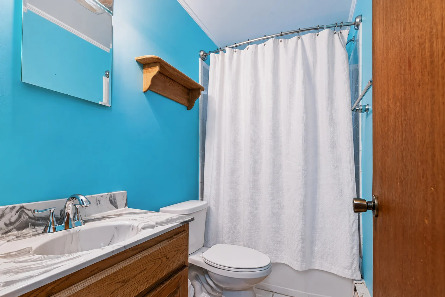 507 Park Ave bathroom with blue walls, a wood vanity and a white shower curtain.