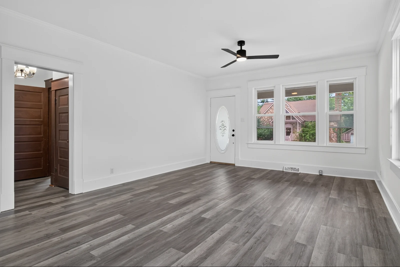 Original empty living room at 915 Shamrock with white walls, a ceiling fan, front windows and gray flooring.