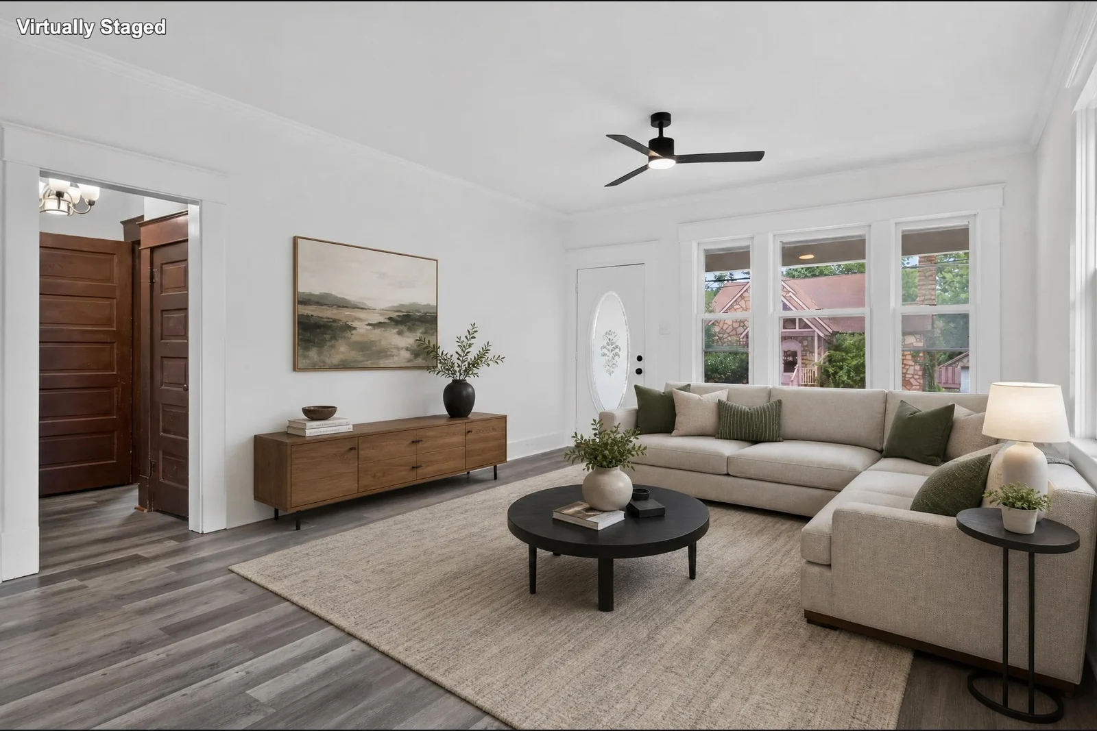Virtually staged version of the same room with a sectional sofa, rug, tables and decor; digitally furnished.